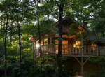 Cabane en bois perchée dans une forêt, éclairée à la tombée du jour
