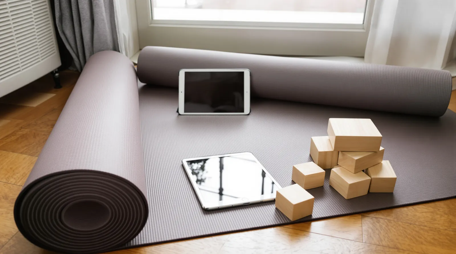 Tapis de yoga, blocs et tablette posés sur un parquet près d'une fenêtre