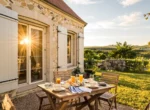 Gîte de campagne en pierre aux volets ouverts, petit-déjeuner servi sur une table en bois